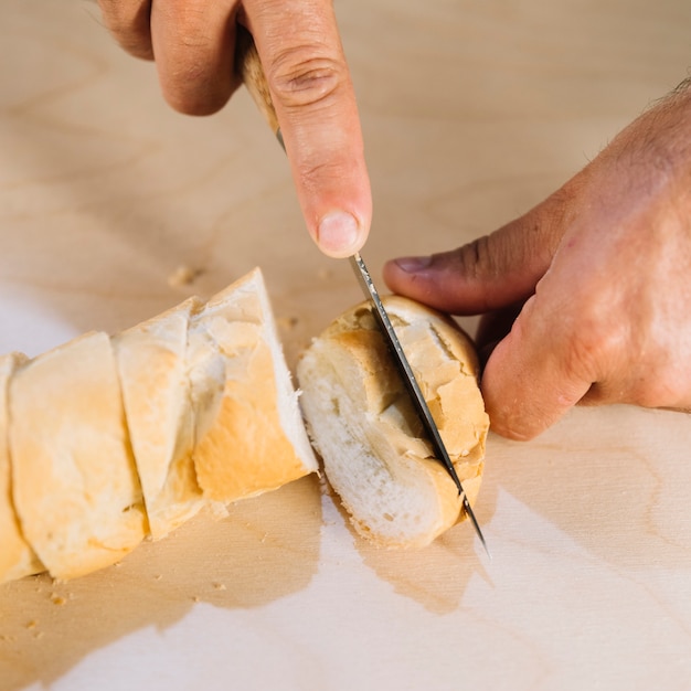 Eine obenliegende Ansicht einer Person, die Brot mit Messer schneidet