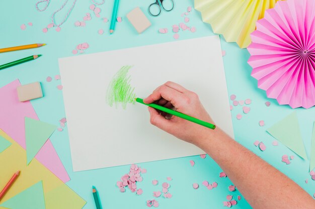Eine obenliegende Ansicht einer Person, die mit grünem Bleistift auf Weißbuch über dem Knickentenhintergrund zeichnet