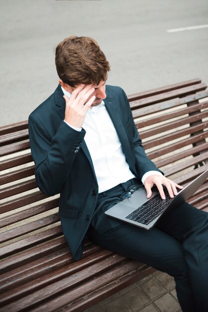 Eine obenliegende Ansicht eines Geschäftsmannes, der auf Bank an der Straße unter Verwendung des Laptops sitzt