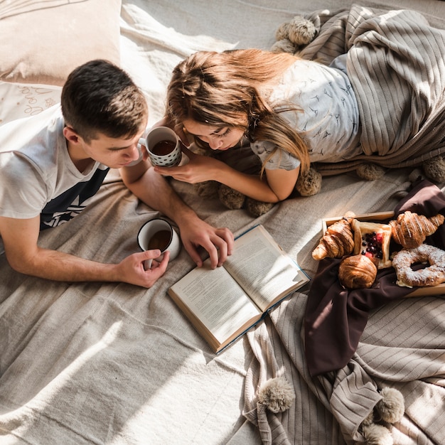 Eine obenliegende Ansicht von den Paaren, die auf dem Bett hält Tasse Kaffee-Lesebuch liegen