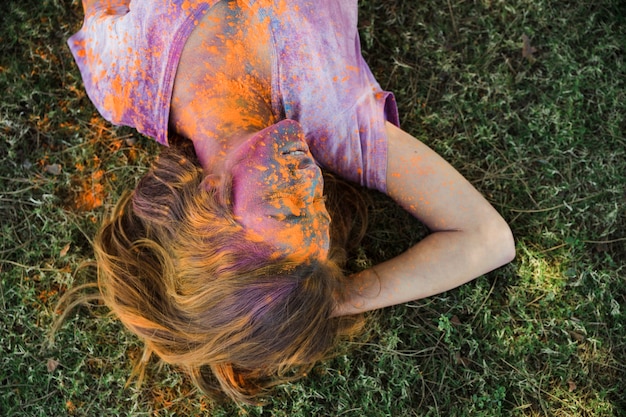Eine orange holi Farbe auf dem Gesicht der Frau, das auf grünem Gras liegt
