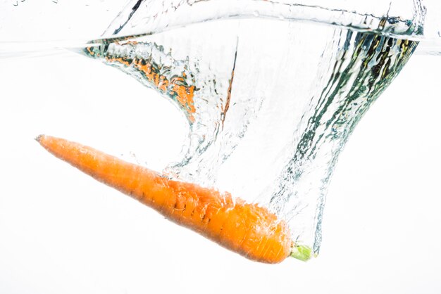 Eine orange Karotte, die im Wasser gegen weißen Hintergrund spritzt