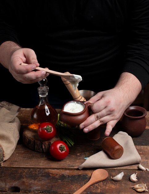 Eine Person, die einen Joghurttopf in den Händen hält Tomaten auf dem Holztisch