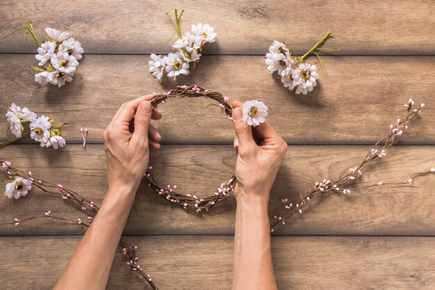 Eine Person, die Kranz mit weißer Blume und den Zweigen auf Holztisch bildet