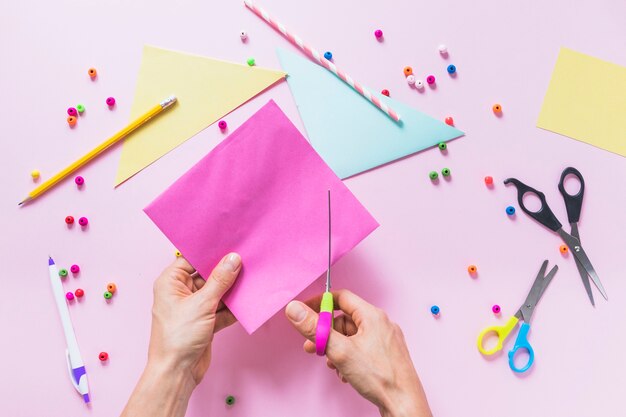 Eine Person, die Papier mit Scissor über dem rosa Hintergrund schneidet