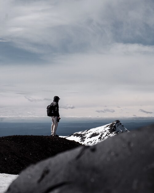 Eine Person, die Rucksack trägt, der oben auf einem Berg unter bewölktem Himmel steht