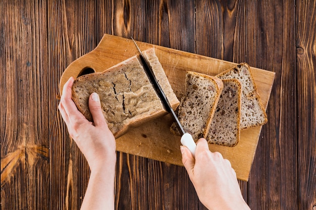 Eine Person, die Scheiben brot mit Messer auf hackendem Brett macht