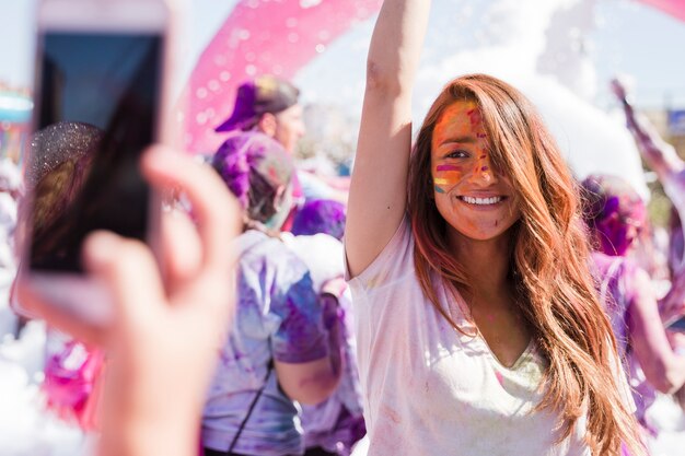 Eine Person, die selfie ihrer lächelnden Freundin am Handy während des holi nimmt