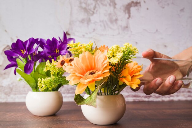 Eine Person, welche die Blumen im Vase auf Holztisch wässert