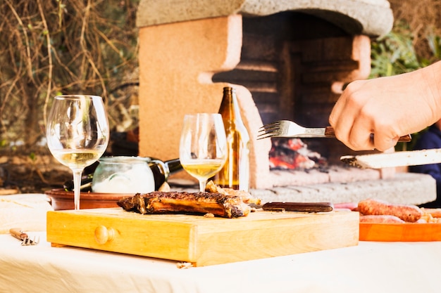 Eine Personenhand, die bereit ist, gegrilltes Fleisch auf hackendem Brett zu essen