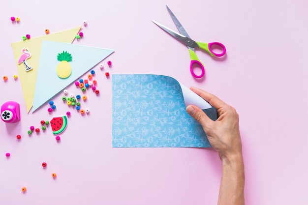 Eine Personenhand, die blaues Papier des Faltens über dem rosa Hintergrund hält