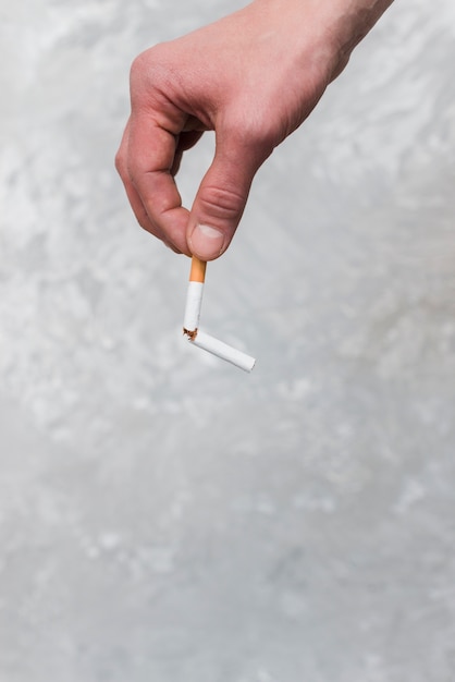 Eine Personenhand, die gebrochene Zigarette auf altem Wandhintergrund hält