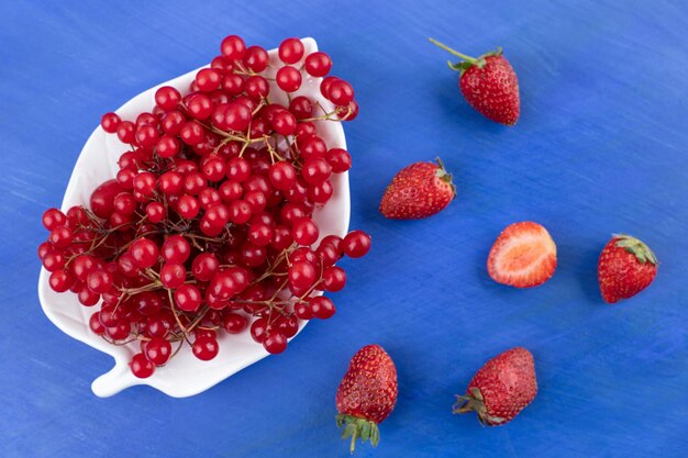 Eine Platte mit roten Johannisbeeren mit ein paar verstreuten Erdbeeren auf blauem Hintergrund. Hochwertiges Foto