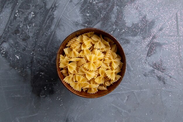 Eine rohe italienische Pasta der Draufsicht, die innerhalb des braunen Tellers auf dem grauen Schreibtischnudelitalienmahlzeitmehl wenig gebildet wird