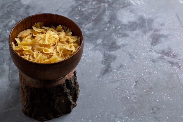 Eine rohe italienische Pasta der Vorderansicht, die wenig innerhalb der braunen Platte auf dem grauen Tischnudelitalienspeisen gebildet wird