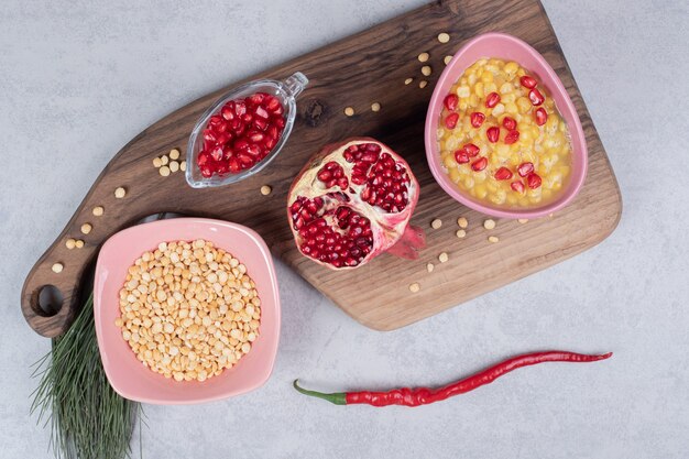 Eine rosa Schüssel voller Linsen mit Granatapfelscheibe auf Holzbrett.