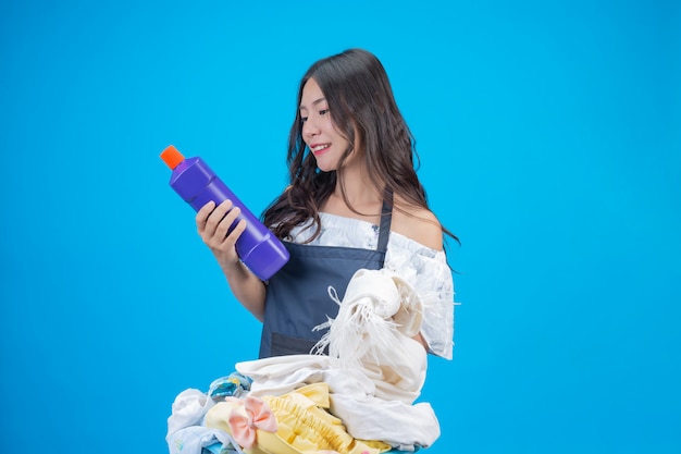 Eine schöne Frau, die ein Tuch und ein flüssiges Reinigungsmittel anhält, bereitete sich für das Waschen auf Blau vor
