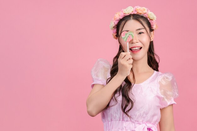 Eine schöne Frau, die in einer rosa Prinzessin gekleidet wird, spielt mit ihrer süßen Süßigkeit auf einem Rosa.