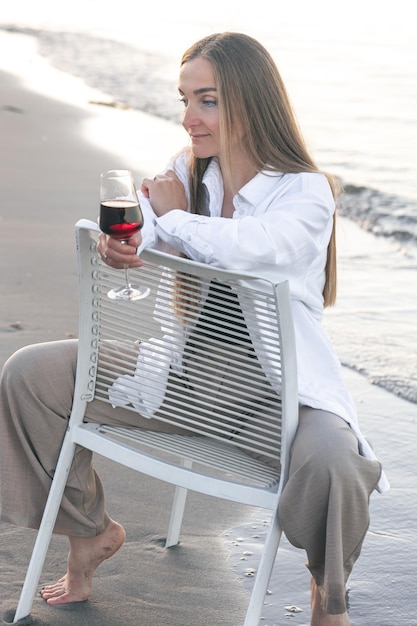 Eine schöne Frau mit einem Glas Wein am Meer sitzt auf einem Stuhl