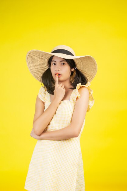 Eine schöne, fröhliche junge Frau mit einem großen Hut auf einem gelben.