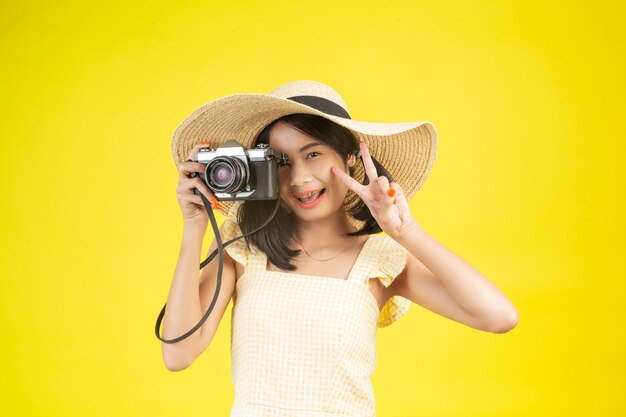 Eine schöne, glückliche Frau, die einen großen Hut und eine Kamera auf einem Gelb trägt.