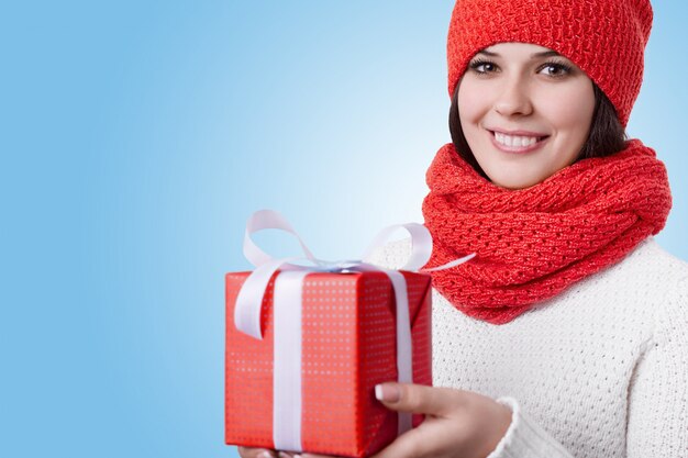 Eine schöne junge Frau mit attraktivem Lächeln und schönen braunen Augen, die roten Hut mit Schal und weißem Pullover tragen