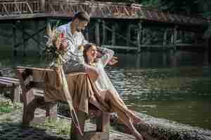 Kostenloses Foto eine schöne junge frau mit blumen und ihr mann sitzen auf einer bank und genießen die kommunikation, ein date in der natur, romantik in der ehe.