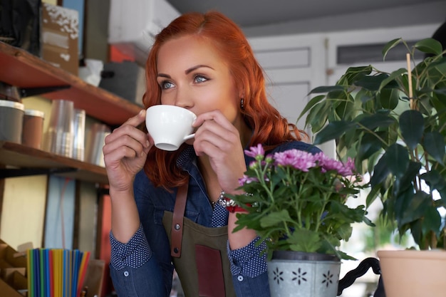 Eine schöne Rothaarige Barista trinkt einen Kaffee im Café.