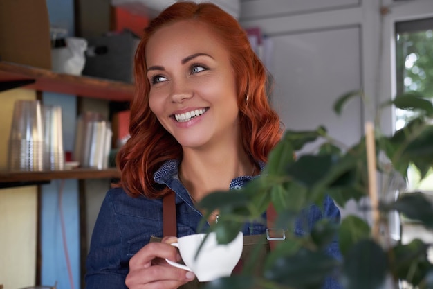 Eine schöne Rothaarige Barista trinkt einen Kaffee im Café.