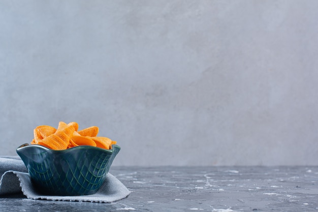 Eine Schüssel mit knusprigen Kartoffelchips auf einem Stück Stoff, auf der Marmoroberfläche