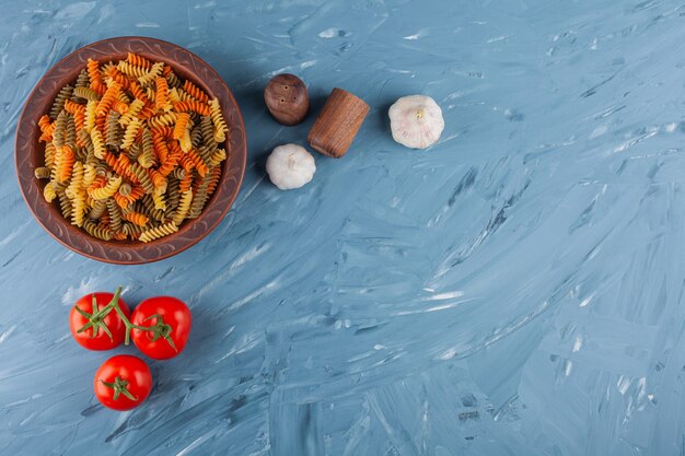 Eine Schüssel mit mehrfarbigen rohen Spiralnudeln mit frischen roten Tomaten und Gewürzen.