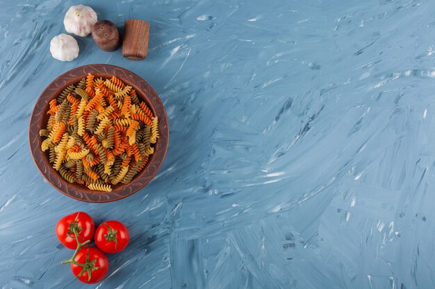 Eine schüssel mit mehrfarbigen rohen spiralnudeln mit frischen roten tomaten und knoblauch.