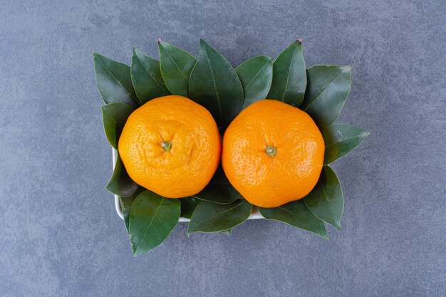 Eine Schüssel mit Orangen und Blättern auf der dunklen Oberfläche