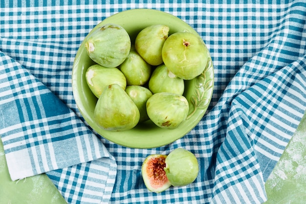 Eine Schüssel mit saftigen grünen Feigen und Feigenscheiben auf blauer Tischdecke.