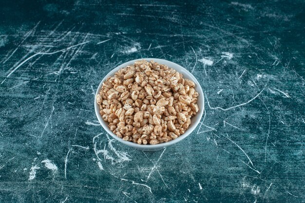 Eine Schüssel mit trockenen Cornflakes auf blauem Hintergrund. Foto in hoher Qualität