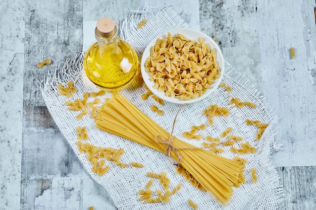 Eine Schüssel mit ungekochten Nudeln und Spaghetti mit Öl und Tischdecke.