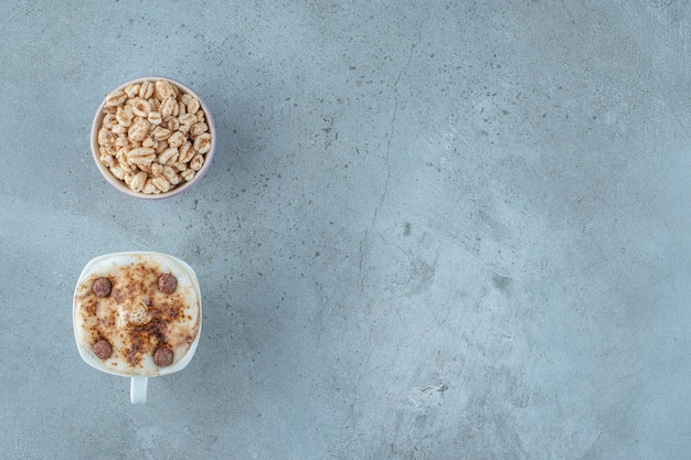 Eine Schüssel Müsli und eine Tasse Cappuccino auf blauem Hintergrund.