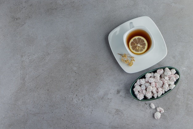 Eine Schüssel voll süßer weißer Bonbons mit einer Tasse heißem Tee auf einem Steintisch.