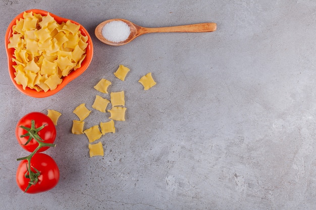 Eine Schüssel voller ungekochter Ravioli-Nudeln mit roten frischen Tomaten und Salz.