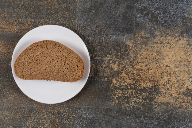 Eine Schwarzbrotscheibe auf weißem Teller.