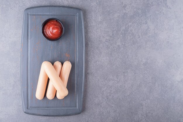 Eine schwarze Tafel mit gekochten Würstchen mit Ketchup