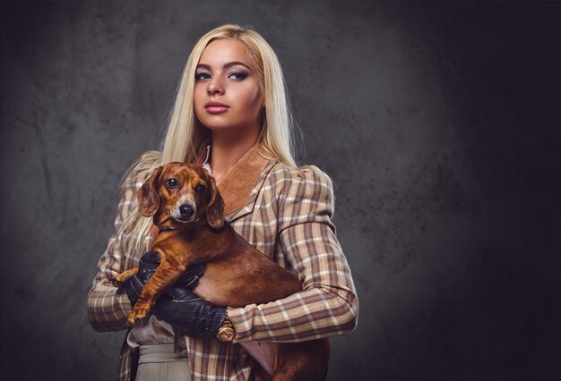 Eine stilvolle blonde Frau in altmodischer Jacke hält einen roten Dachshund.