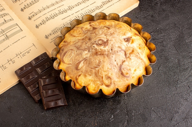 Eine süße Ansicht des süßen runden Kuchens der Draufsicht innerhalb der Kuchenform zusammen mit Schokoriegeln auf dem grauen Hintergrundkekszuckerplätzchen