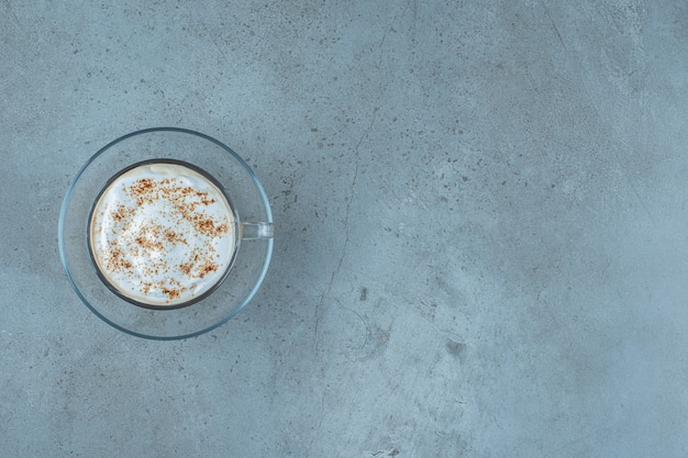 Eine Tasse Cappuccino auf einer Untertasse, auf blauem Hintergrund.