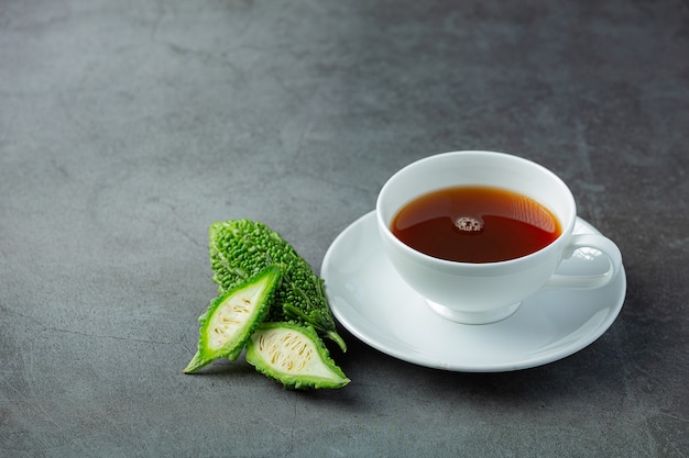 eine Tasse heißen bitteren Kürbistee mit geschnittenem rohem bitterem Kürbis auf dunklem Boden