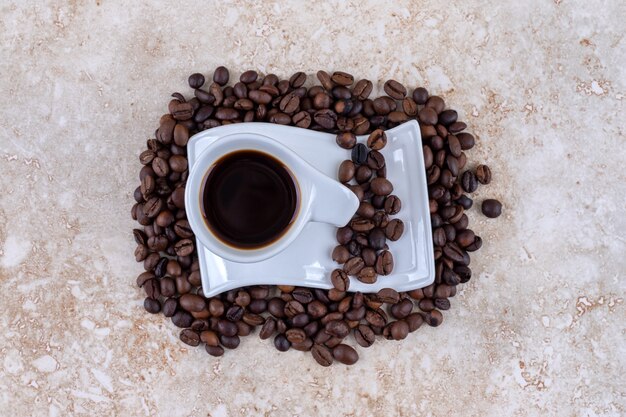 Eine Tasse Kaffee auf einer Untertasse, die auf einem Stapel Kaffeebohnen sitzt