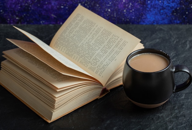 Eine tasse kaffee mit buch auf einer dunklen oberfläche.