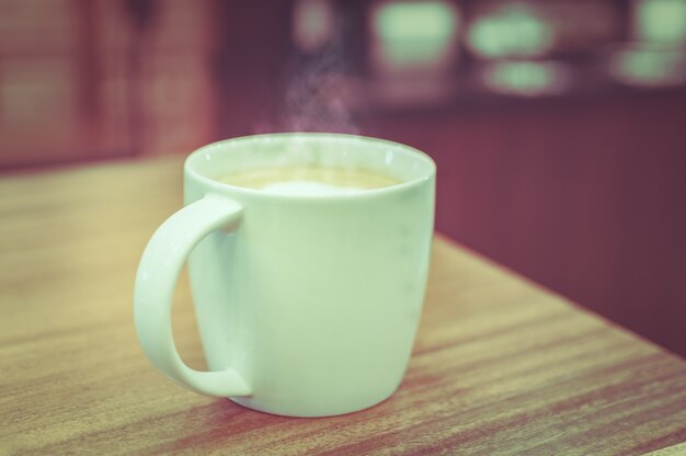 Eine Tasse Kaffee mit Herzmuster in einer weißen Tasse auf hölzernen background.Vintage Ton.