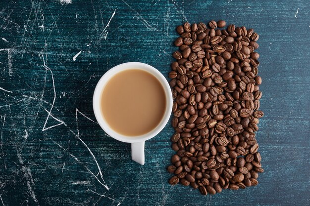 Eine Tasse Kaffee mit Körnern auf blauer Oberfläche.