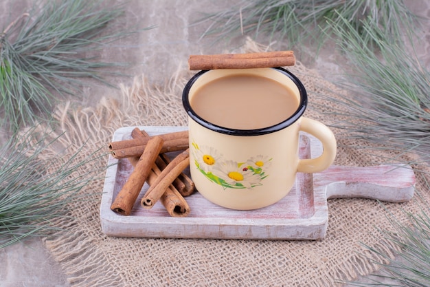 Eine Tasse Kaffee mit Zimtstangen auf rustikalem Holzbrett.